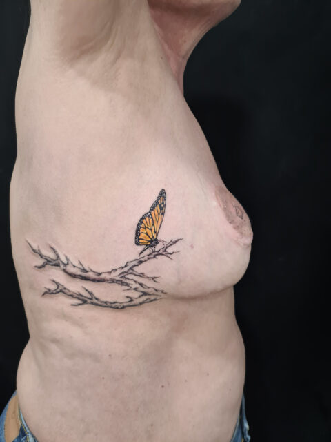Tatuaje reparador sobre cicatriz en el pecho con unas ramas de cerezo y una mariposa